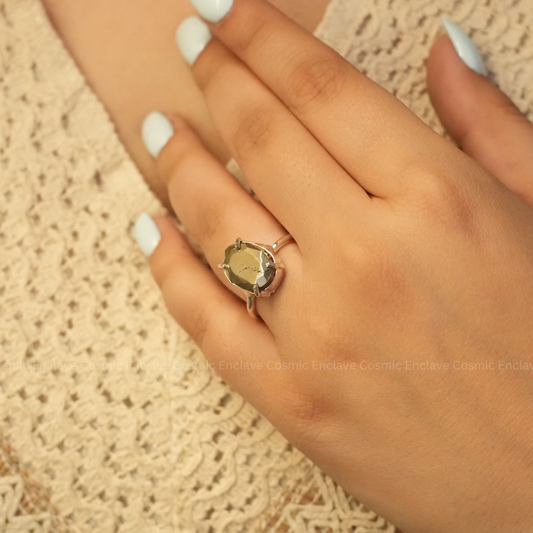 A hand showcasing a silver-colored ring with a precision-cut pyrite gemstone on the finger.