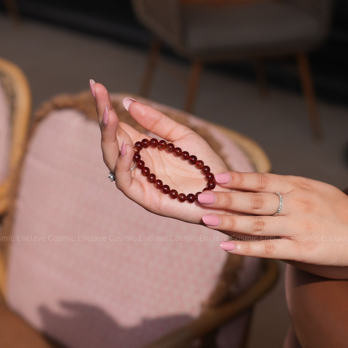 Person holding a red beaded Hessonite bracelet in their hand with a blurred background