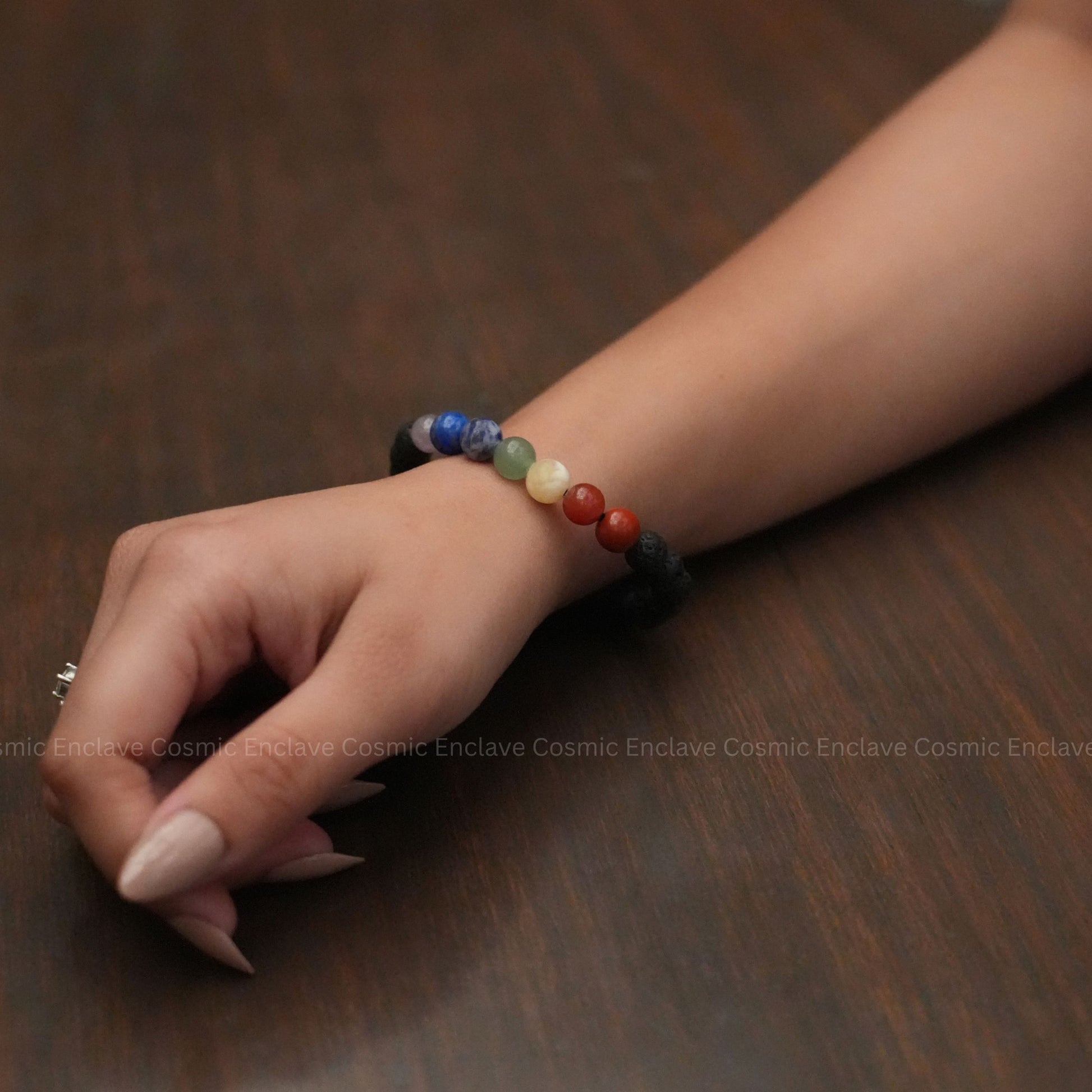 Close-up of a hand wearing a colorful 7 Chakra  beaded bracelet on a wooden surface