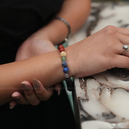 Close-up of a wrist wearing a colorful 7 Chakra beaded bracelet with a blurred background.