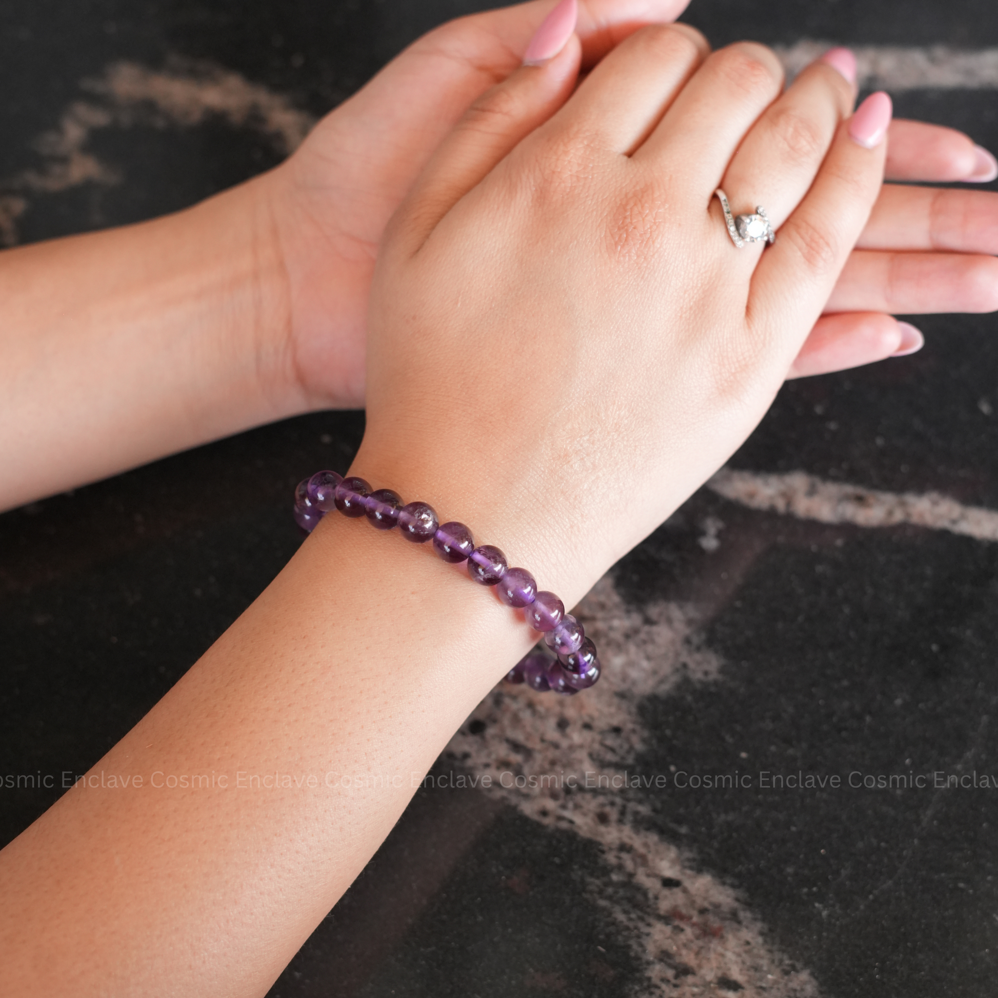 A person's hands holding a beaded bracelet made of purple amethyst stones.