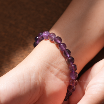 A person's hands holding a beaded bracelet made of purple amethyst stones.