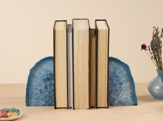 A pair of blue agate bookends on a wooden surface, holding up three books, with a vase and decorative items in the background.