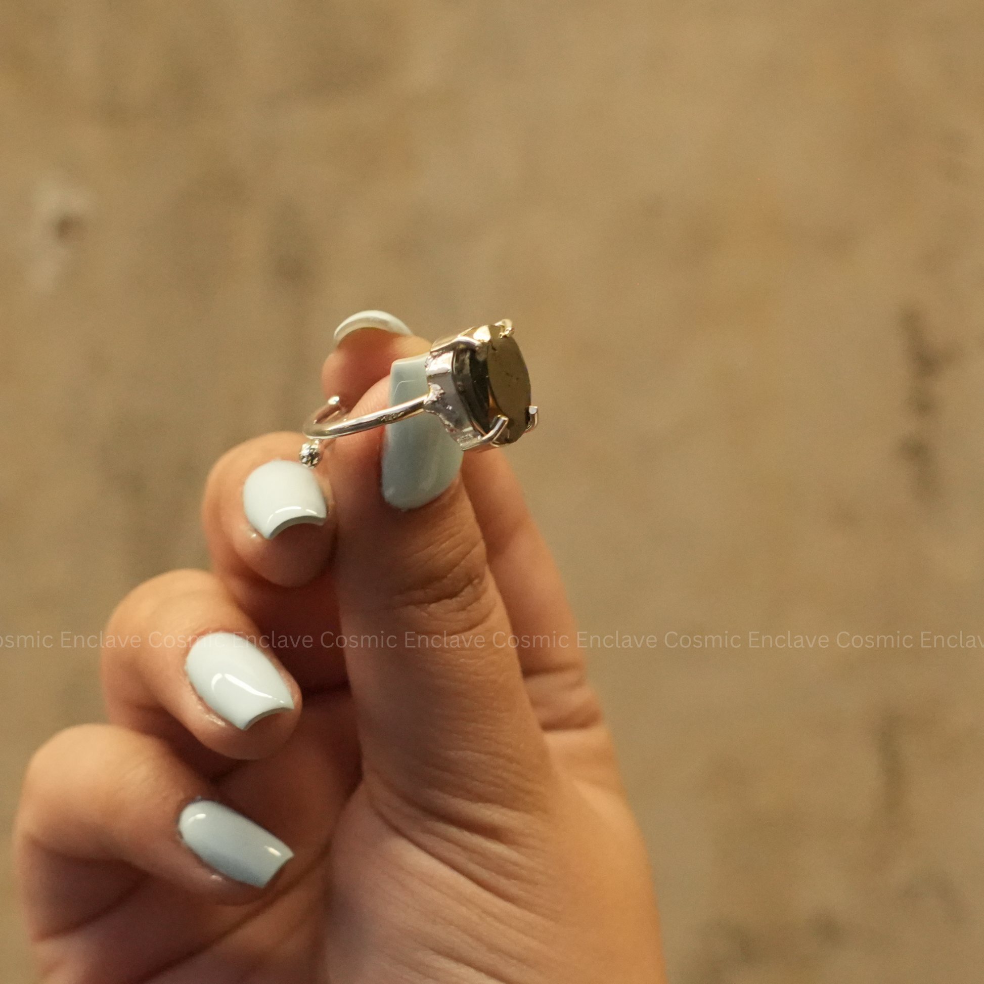 A hand showcasing a silver-colored ring with a precision-cut pyrite gemstone on the finger.