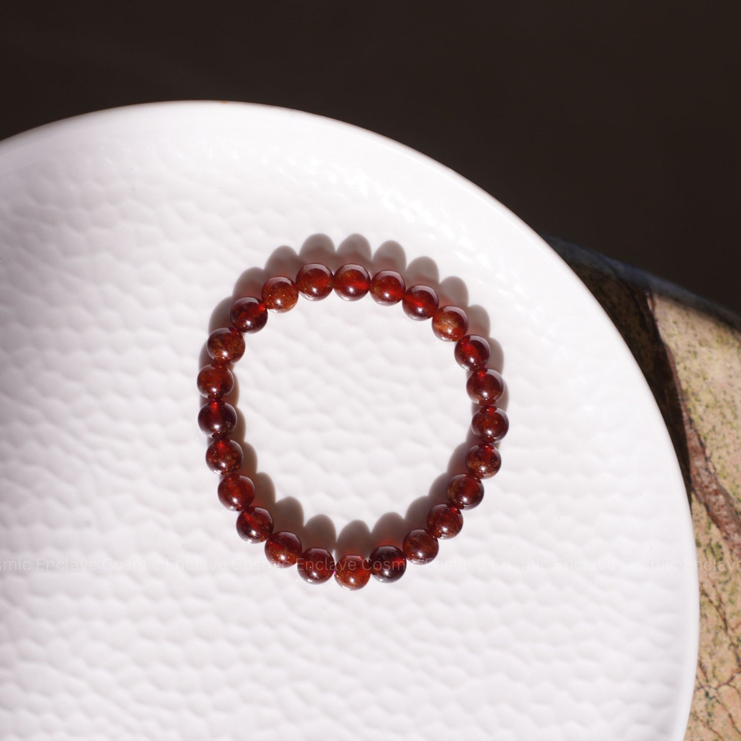 Red beaded Hessonite bracelet on a white surface with a dark background