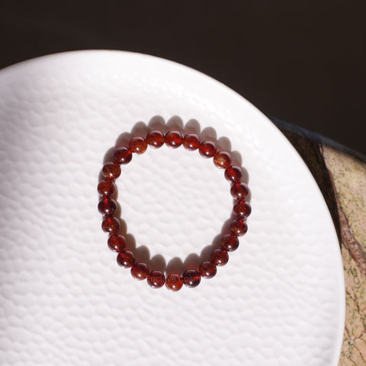 Red beaded Hessonite bracelet on a white surface with a dark background