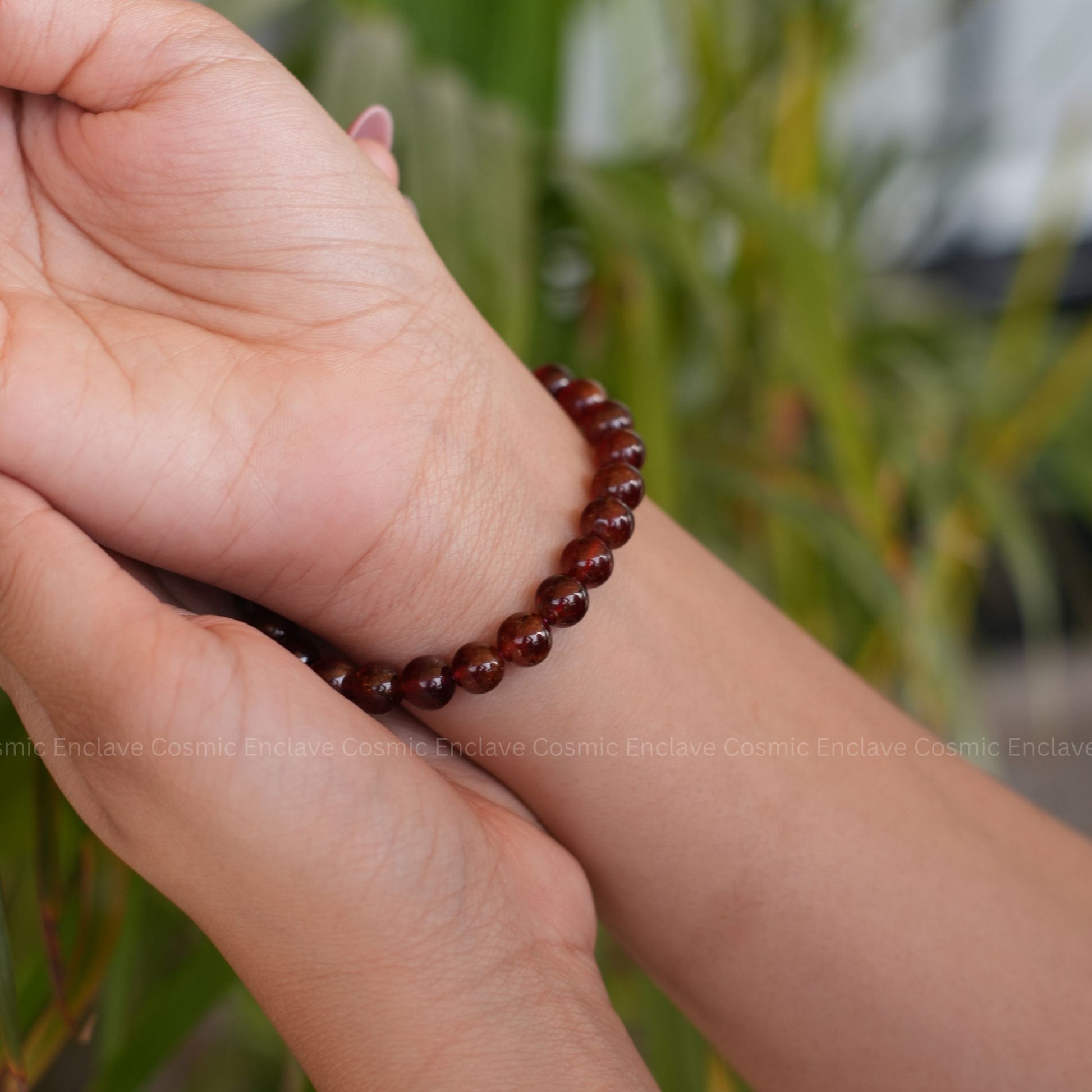 Hand wearing a red beaded Hessonite bracelet with a blurred green background