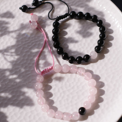 Two beaded bracelets, one black Tourmaline and one Rose Quartz, on a textured white surface.
