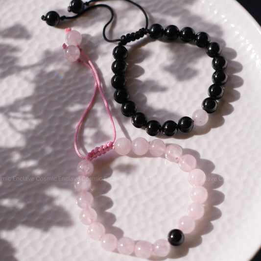 Two beaded bracelets, one black Tourmaline and one Rose Quartz, on a textured white surface.