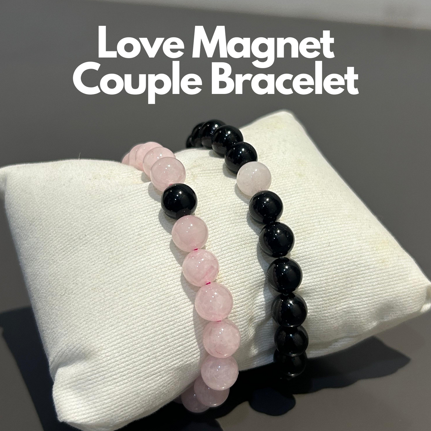 Two beaded bracelets, one with pink rose quartz and the other with black tourmaline, displayed on a white cushion with the text 'Love Magnet Couple Bracelet' above.