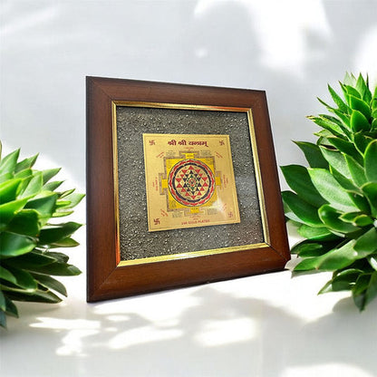 A framed Pyrite Lakshmi Yantra, a sacred symbol of abundance, displayed against a neutral background with green plants to the side. Used for attracting wealth. this is a perfect piece for home decor and gifting too. 