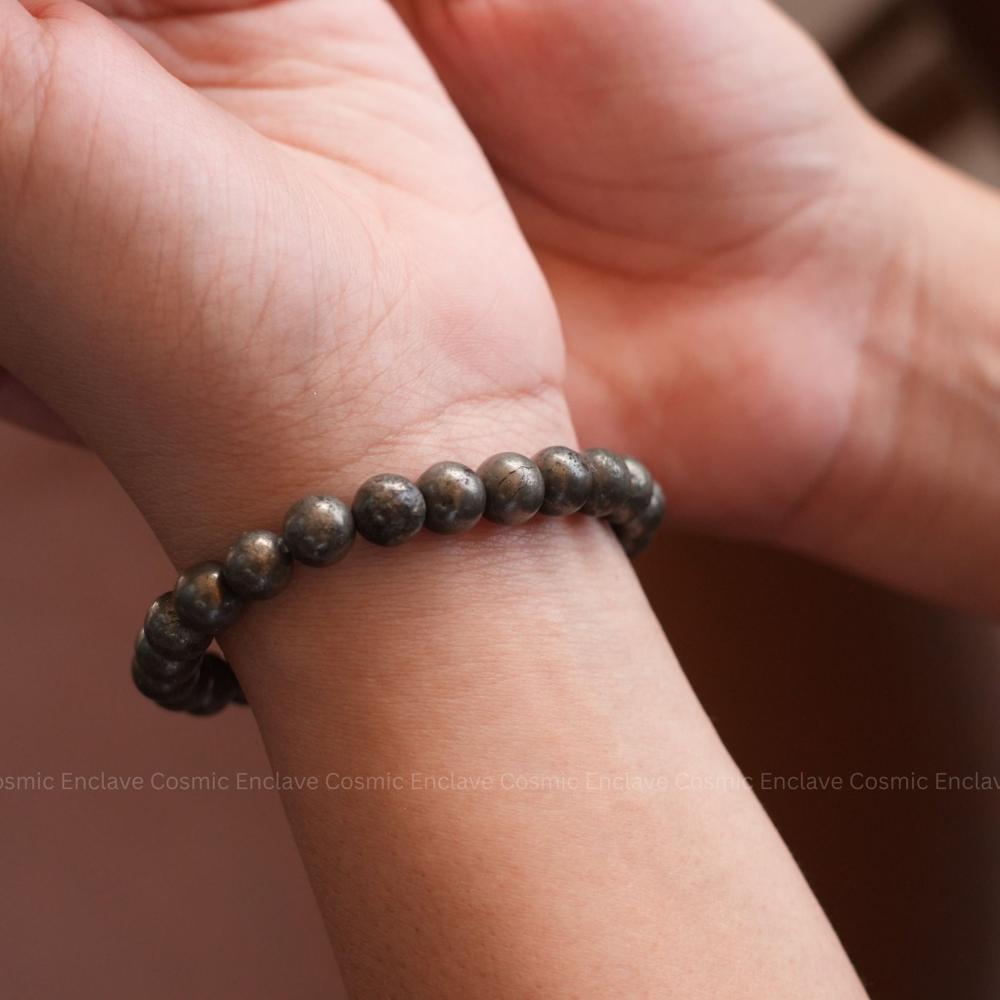 Close-up of a hand wearing a Pyrite beaded bracelet on a blurred background
