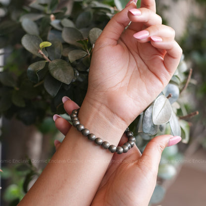 Hand wearing a Pyrite beaded bracelet with a blurred green leafy background