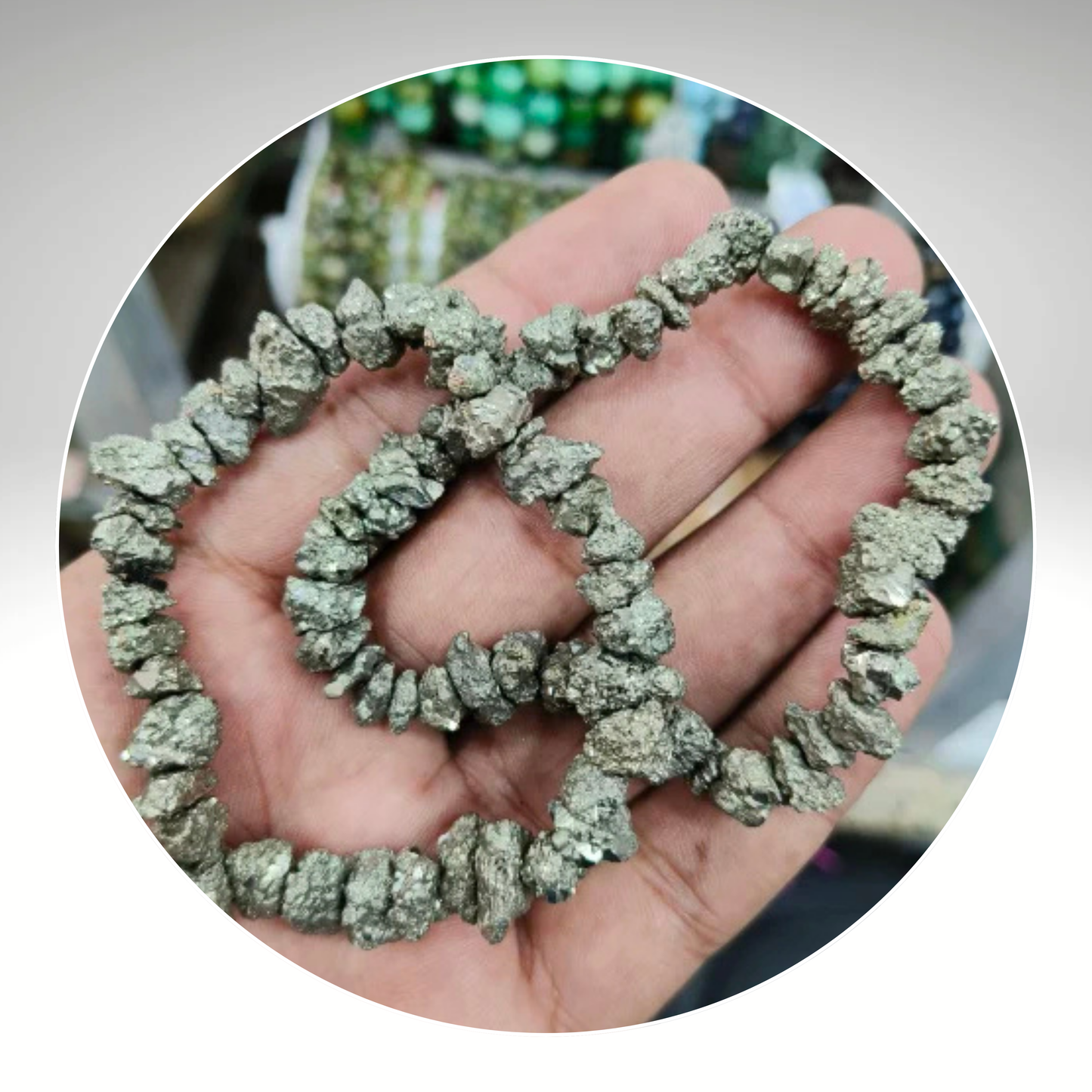 A hand holding a bracelet made of pyrite chips, with a blurred background. Known for Attracting Wealth and Abundance.