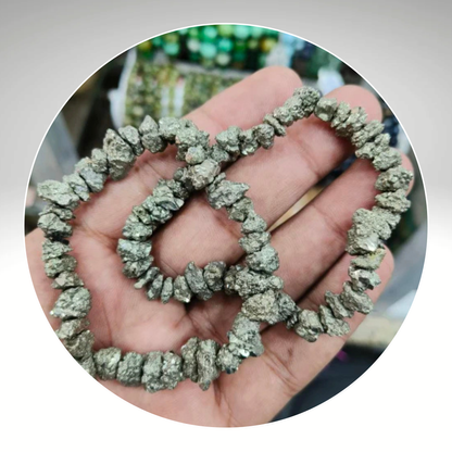 A hand holding a bracelet made of pyrite chips, with a blurred background. Known for Attracting Wealth and Abundance.