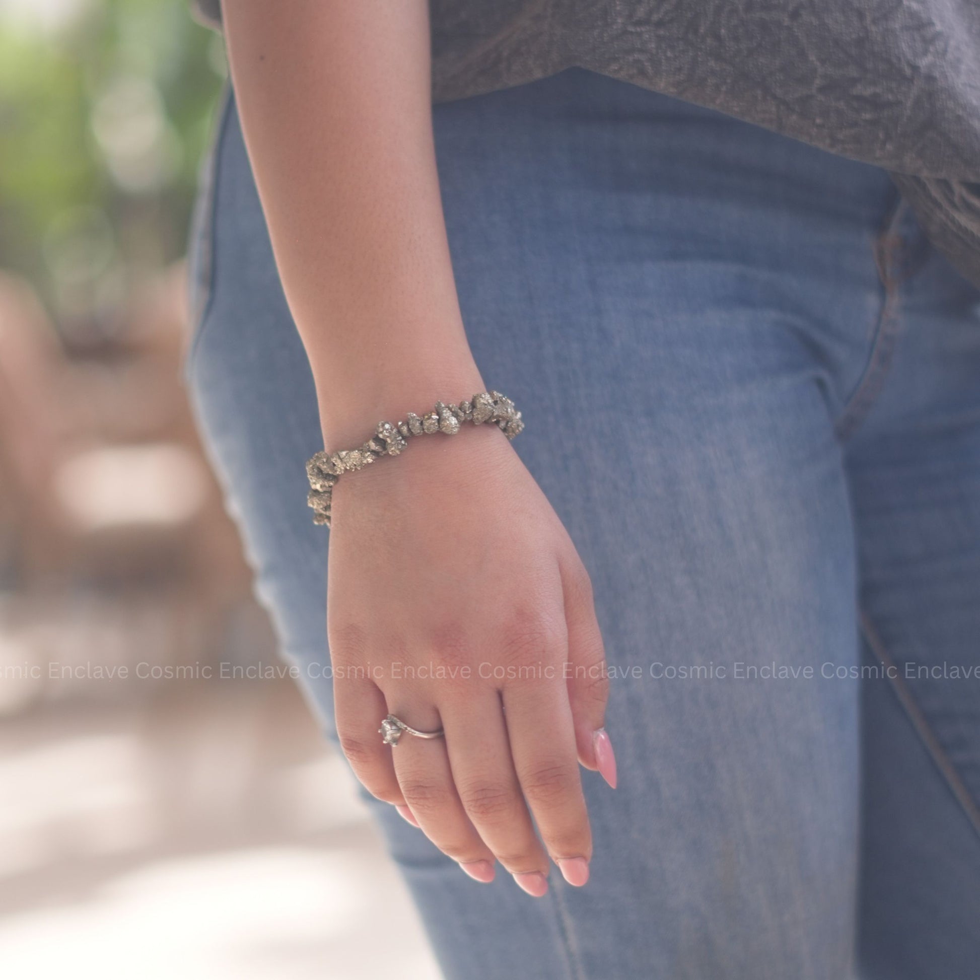 Close-up of a hand wearing a Pyrite bracelet and ring with a blurred background