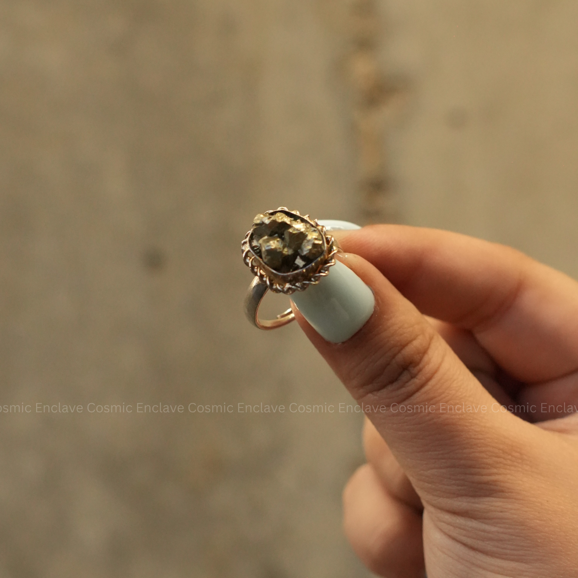A hand holding a ring with a large, square-shaped pyrite stone set in a gold-colored mounting.