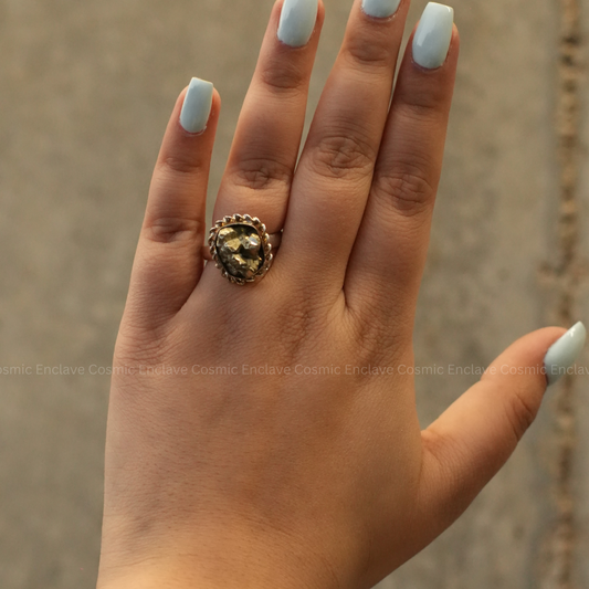 A hand with a ring with a large, square-shaped pyrite stone set in a gold-colored mounting.