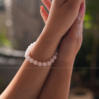 Hand wearing a pink beaded Rose Quartz bracelet with a blurred background