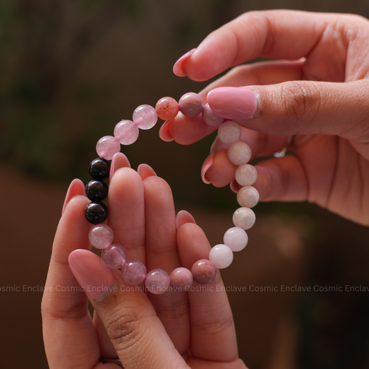 A person holding a bracelet composed of round beads in shades of pink, black, and white. Known for attracting Love in life.
